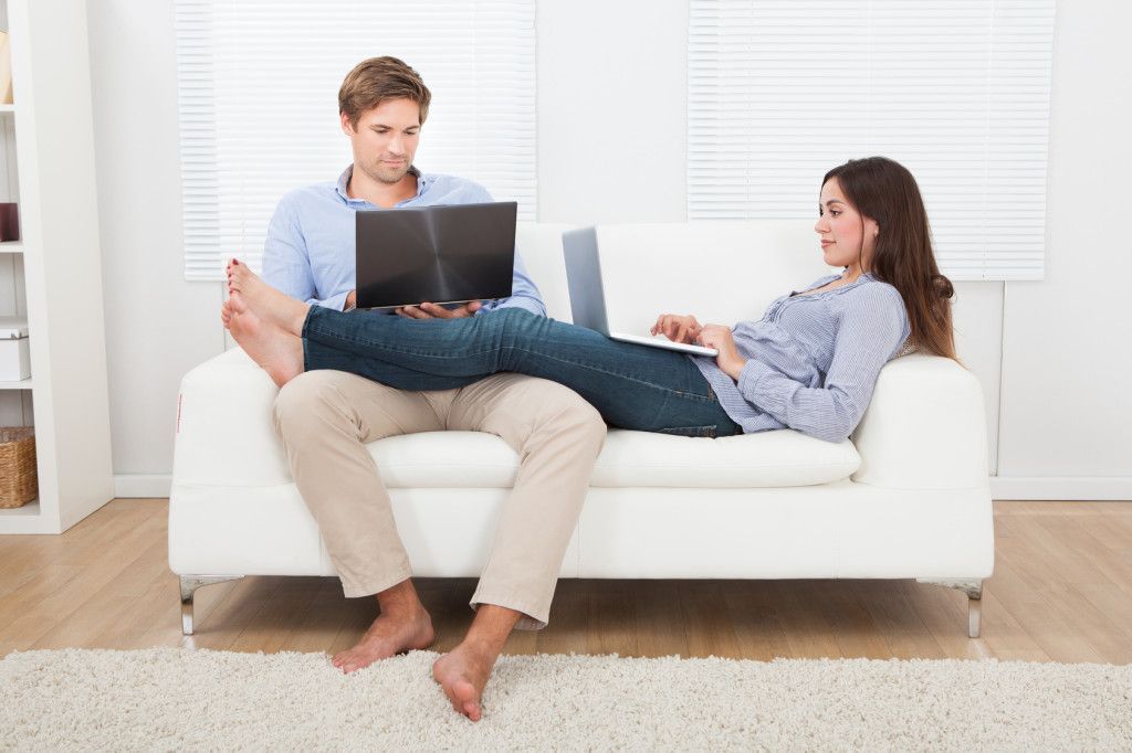 Couple Using Laptops On Sofa